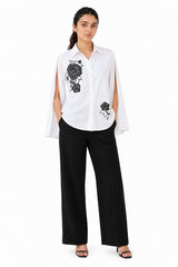 Crisp white shirt featuring bold black floral embroidery, a classic collar, button-down front, and dramatic open-cut sleeves.